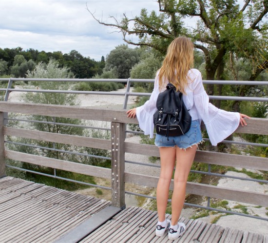 Bell Sleeve Blouse. Fashion Blogger Girl by Style Blog Heartfelt Hunt. Girl with blond beach waves wearing a white bell sleeve blouse, denim shorts, backpack and adidas sneakers.