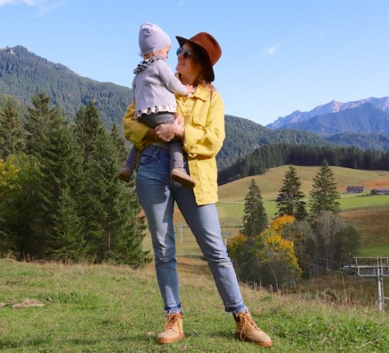 Fall Trip. Fashion Blogger Girl by Style Blog Heartfelt Hunt. Girl with blond, low messy bun wearing a yellow denim jacket, flower T-shirt, brown hat, Ray-Ban sunglasses, Michael Kors backpack, mom jeans and boots.