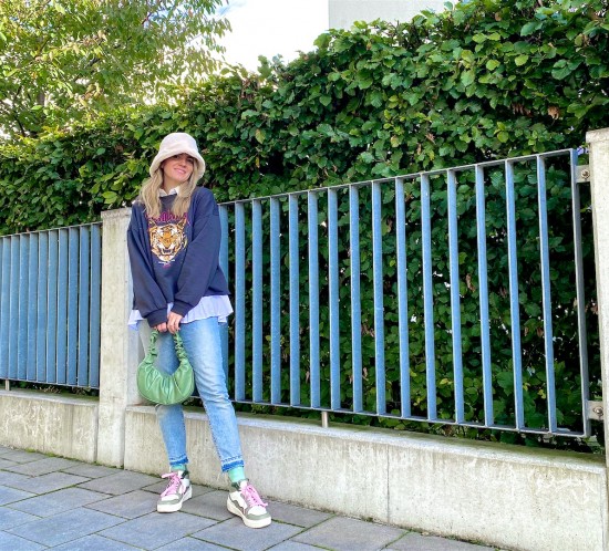 Faux Fur Hat. Fashion Blogger Girl by Style Blog Heartfelt Hunt. Girl with blond hair wearing a faux fur hat, sweatshirt, mom jeans, green ruched bag and green sneakers.