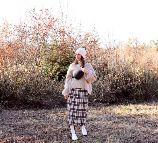 Forest Walk. Fashion Blogger Girl by Style Blog Heartfelt Hunt. Girl with blond hair wearing a pompom beanie, white turtleneck, chunky sweater, pleated skirt, belt bag and white boots.