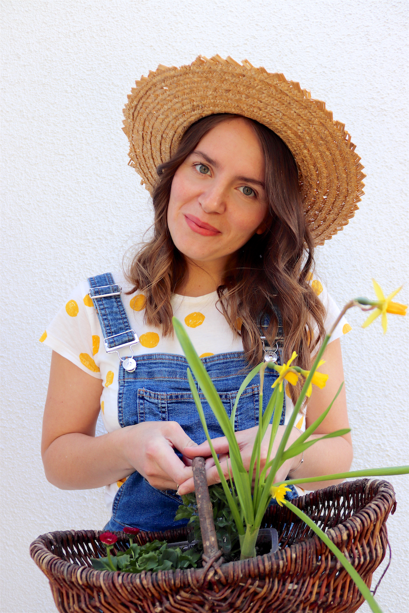 Gardening. Fashion Blogger Girl by Style Blog Heartfelt Hunt. Girl with blond, loose curls wearing a straw hat, yellow polka dot tee and denim overall.