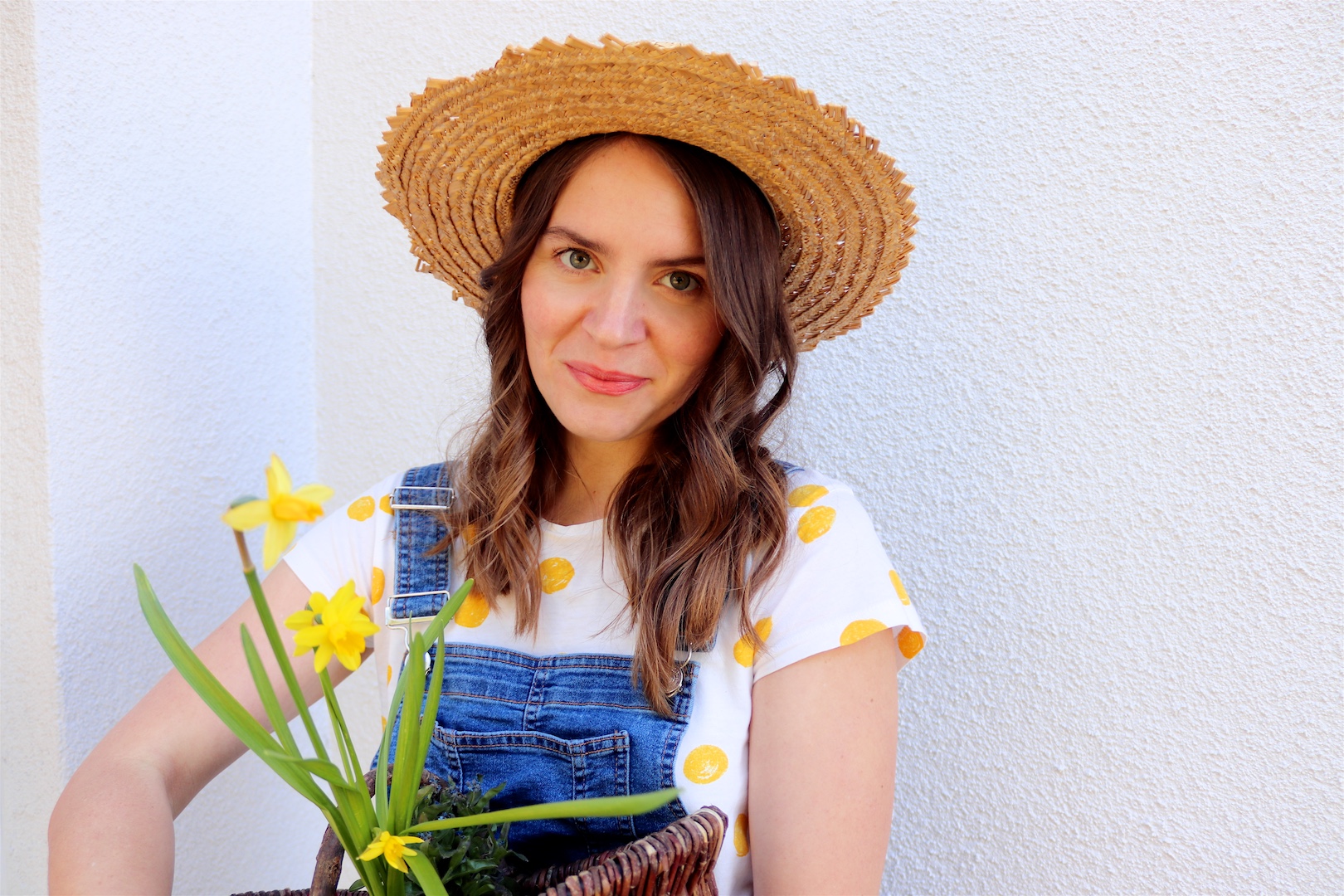 Gardening. Fashion and Style Blog Girl from Heartfelt Hunt. Girl with blonde, loose curls wearing a straw hat, yellow polka dot tee and denim overall.