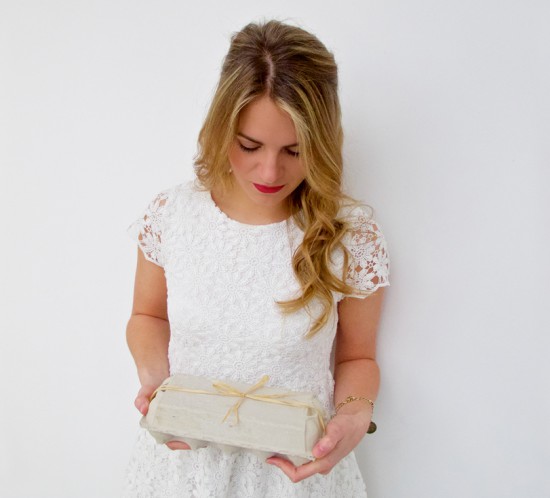 Blonde fashion and style blogger girl in closeup view holding an egg carton with a bow, wearing a romantic, white lace dress and red lipstick