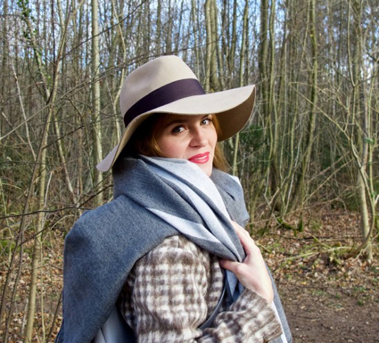 Smiling blonde fashion and style blogger girl in closeup view with floppy hat, oversized scarf, plaid jacket and red lips in the woods