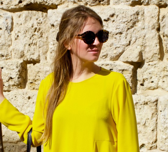 Smiling blonde fashion and style blogger girl wearing a colorful, yellow dress and sunglasses in the beautiful old town of Marbella