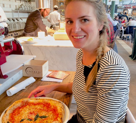 Smiling blonde fashion and style blogger girl with braided hair in closeup view eating pizza, wearing a striped top with bow
