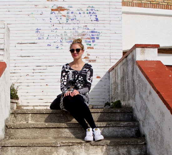 Blonde fashion and style blogger girl sitting on stairs, wearing a lace dress, Michael Kors bag, Rayban sunglasses and adidas sneakers