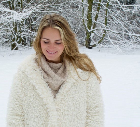 Smiling blonde fashion and style blogger girl in closeup view wearing a teddy bear coat with hood in a winter wonderland
