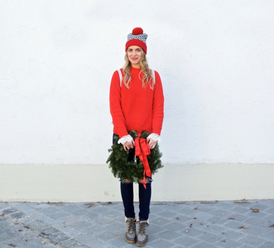 Holiday Wreath. Fashion Blogger Girl by Style Blog Heartfelt Hunt. Girl with blond, loose curls wearing a red sweater, lace top with bell sleeves, destroyed jeans, pompom beanie, backpack and boots.