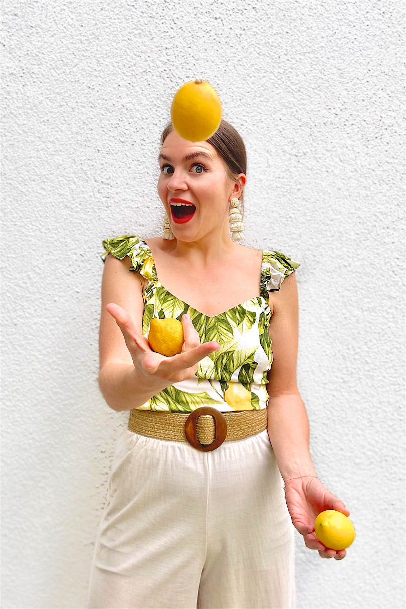 Lemon Print. Fashion and Style Blog Girl from Heartfelt Hunt. Girl with blonde, low bun wearing a lemon print top, tassel earrings, straw belt and beige pants.