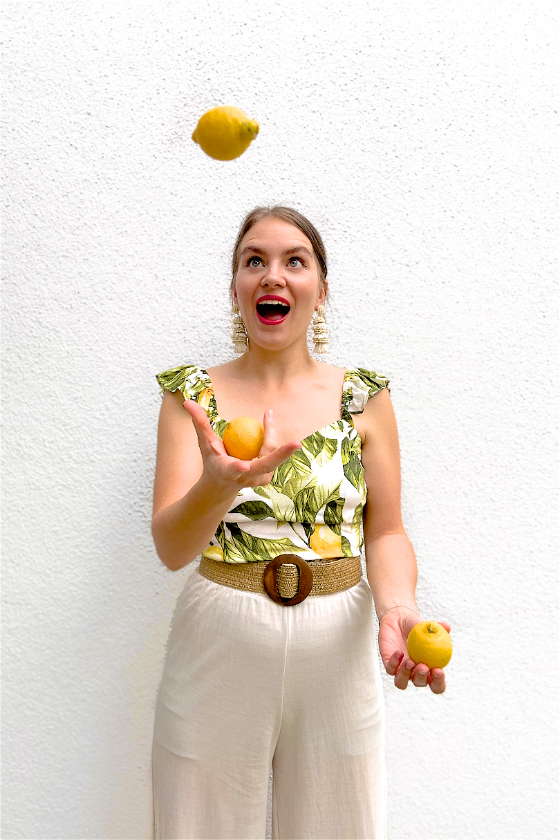 Lemon Print. Fashion and Style Blog Girl from Heartfelt Hunt. Girl with blonde, low bun wearing a lemon print top, tassel earrings, straw belt and beige pants.