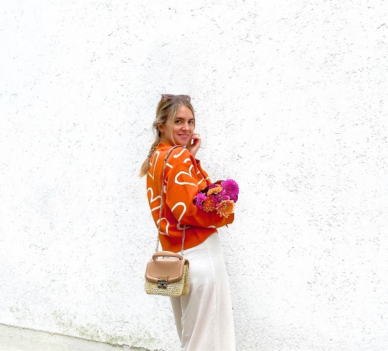 Orange Cardigan. Fashion Blogger Girl by Style Blog Heartfelt Hunt. Girl with blond dutch braid wearing an orange cardigan, wide leg pants, slim sunglasses, straw bag, orange socks and chunky sneakers.