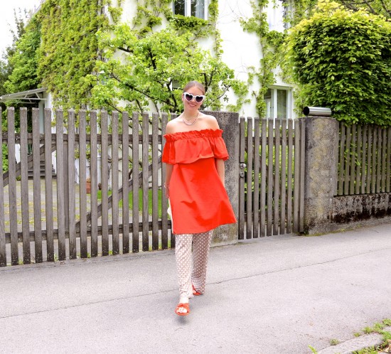 Orange & Polka Dots. Fashion Blogger Girl by Style Blog Heartfelt Hunt. Girl with blond, low bun wearing an orange off-shoulder dress, polka dot pants, white heart shaped sunglasses, pearl bag and orange sandals.