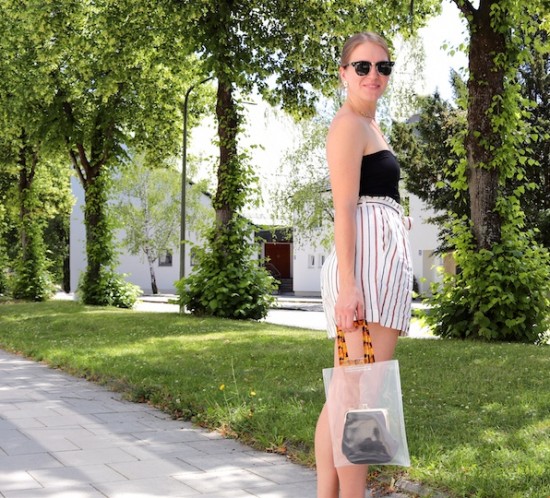 Paperbag Shorts. Fashion Blogger Girl by Style Blog Heartfelt Hunt. Girl with blond hair wearing paperbag shorts, black top, Ray-Ban sunglasses, pearl earrings, transparent bag and black sandals.