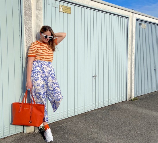Pattern Mix. Fashion Blogger Girl by Style Blog Heartfelt Hunt. Girl with blond hair wearing a striped T-shirt, floral pants, white slim sunglasses, orange Michael Kors bag, colorful socks and chunky sneakers.