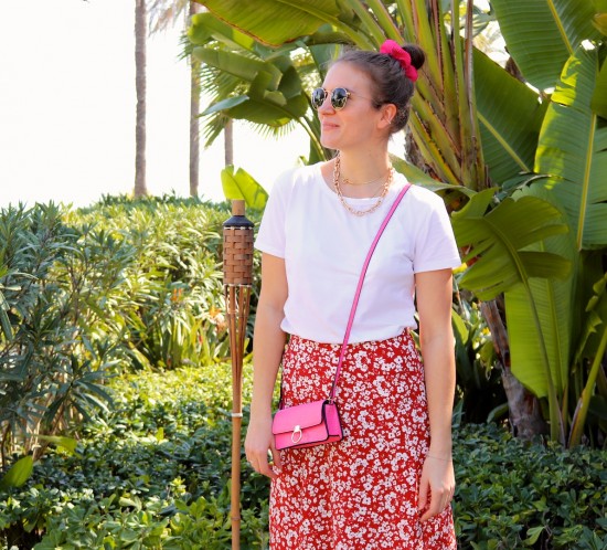 Pink Floral. Fashion Blogger Girl by Style Blog Heartfelt Hunt. Girl with blond, high, messy bun and pink scrunchie wearing a pink bag, Ray-Ban sunglasses, floral skirt, statement necklace, white tee and chunky sneakers.