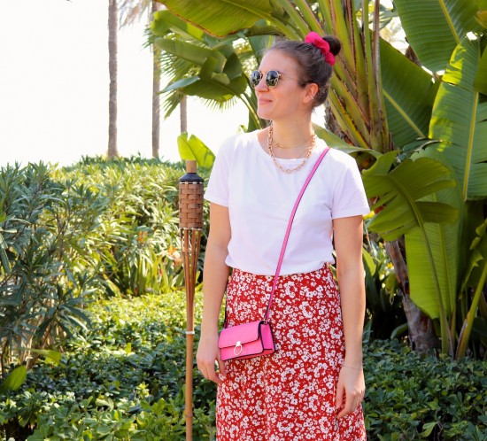 Pink Floral. Fashion Blogger Girl by Style Blog Heartfelt Hunt. Girl with blond, high, messy bun and pink scrunchie wearing a pink bag, Ray-Ban sunglasses, floral skirt, statement necklace, white tee and chunky sneakers.