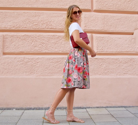 Pink Flowers. Fashion Blogger Girl by Style Blog Heartfelt Hunt. Girl with blond loose curls wearing a White top, skirt with pink flowers, pink bow belt, bag, lace up sandals and sunglasses.