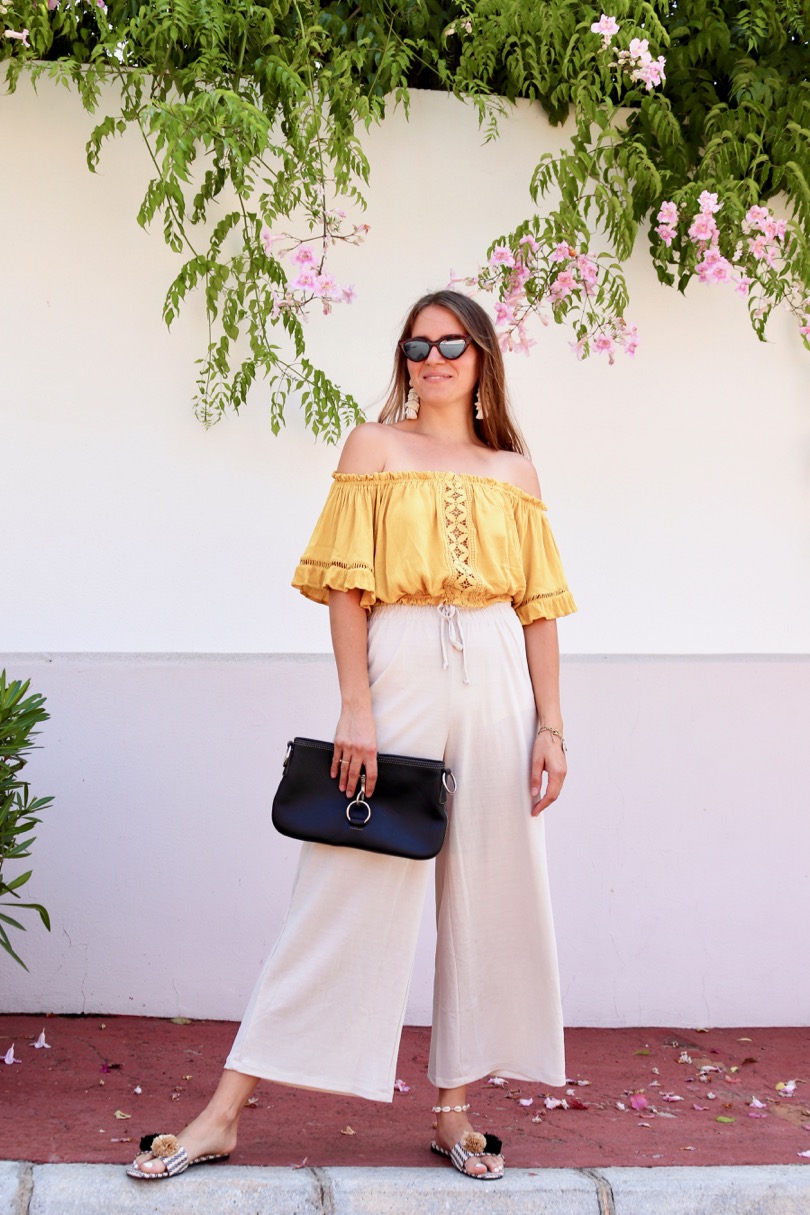 Pompon Straw Sandals. Fashion Blogger Girl by Style Blog Heartfelt Hunt. Girl with blond hair wearing a yellow off shoulder top, wide pants, tortoise shell sunglasses, tassel earrings, clutch and pompon straw sandals.