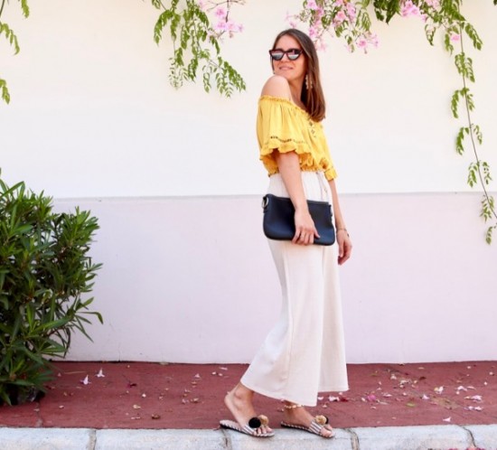 Pompon Straw Sandals. Fashion Blogger Girl by Style Blog Heartfelt Hunt. Girl with blond hair wearing a yellow off shoulder top, wide pants, tortoise shell sunglasses, tassel earrings, clutch and pompon straw sandals.