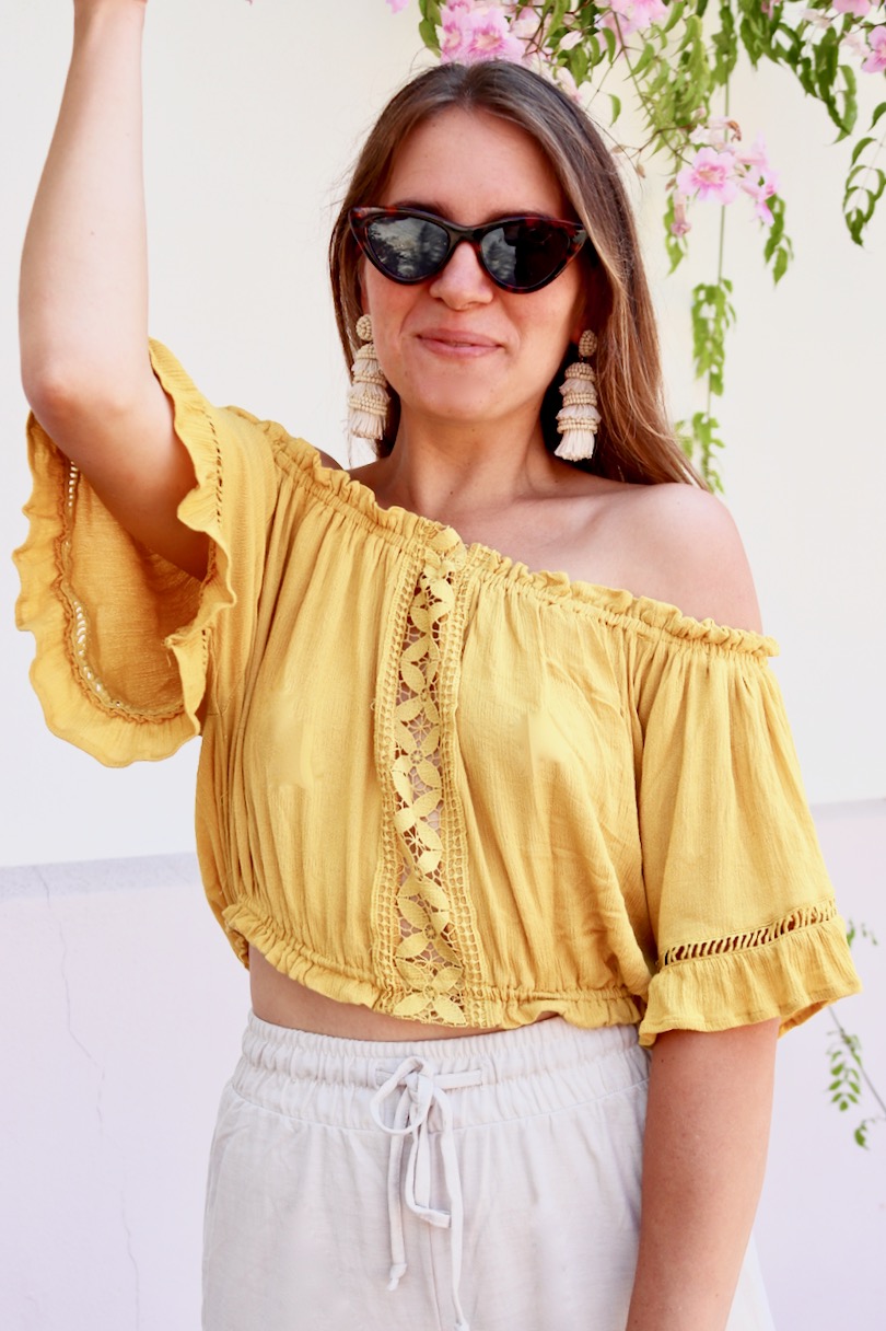 Pompon Straw Sandals. Fashion and Style Blog Girl from Heartfelt Hunt. Girl with blonde hair wearing a yellow off shoulder top, wide pants, tortoise shell sunglasses, tassel earrings, clutch and pompon straw sandals.