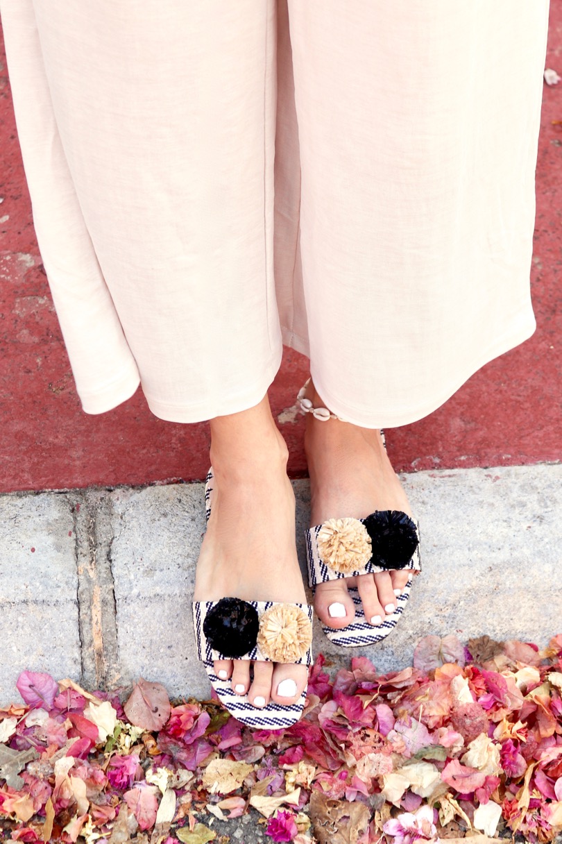 Pompon Straw Sandals. Fashion and Style Blog Girl from Heartfelt Hunt. Girl with blonde hair wearing a yellow off shoulder top, wide pants, tortoise shell sunglasses, tassel earrings, clutch and pompon straw sandals.