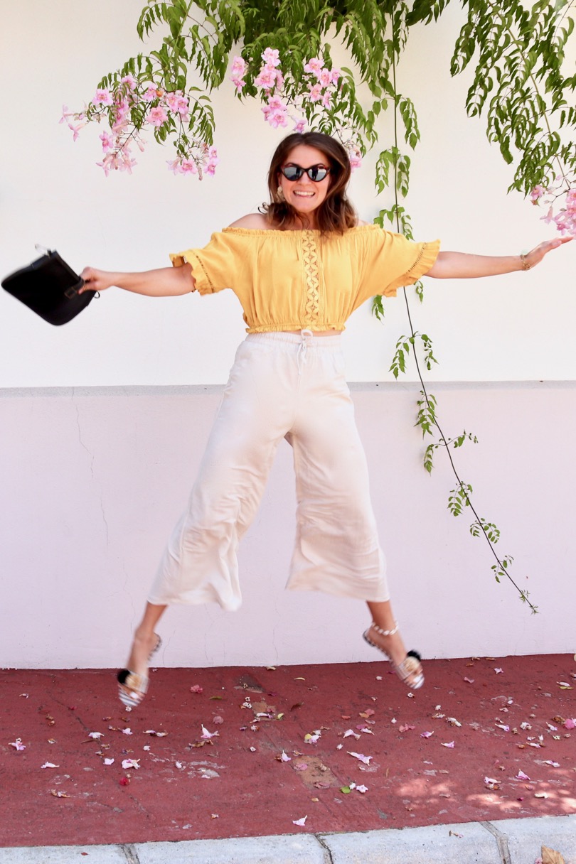 Pompon Straw Sandals. Fashion Blogger Girl by Style Blog Heartfelt Hunt. Girl with blond hair wearing a yellow off shoulder top, wide pants, tortoise shell sunglasses, tassel earrings, clutch and pompon straw sandals.