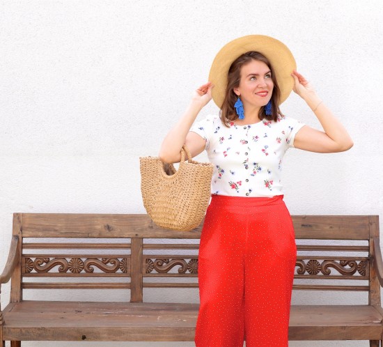 Red Floral. Fashion Blogger Girl by Style Blog Heartfelt Hunt. Girl with blond hair wearing a floral tee, red pants, blue tassel earrings, straw hat, straw bag and straw loafers.