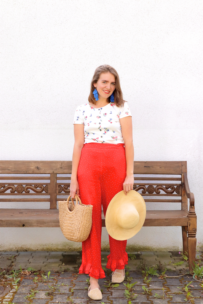 Red Floral. Fashion Blogger Girl by Style Blog Heartfelt Hunt. Girl with blond hair wearing a floral tee, red pants, blue tassel earrings, straw hat, straw bag and straw loafers.