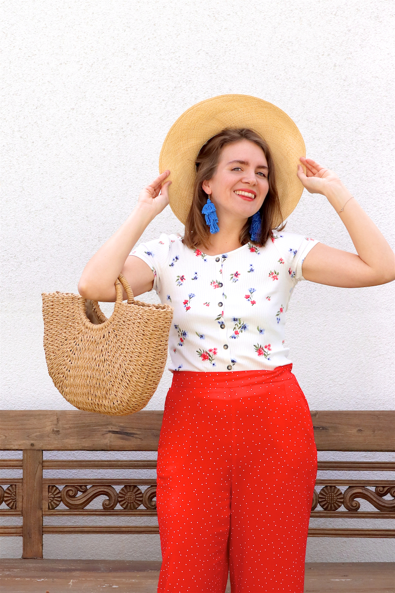 Red Floral. Fashion and Style Blog Girl from Heartfelt Hunt. Girl with blonde hair wearing a floral tee, red pants, blue tassel earrings, straw hat, straw bag and straw loafers.