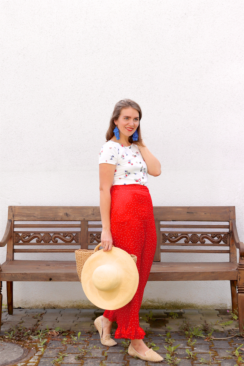 Red Floral. Fashion Blogger Girl by Style Blog Heartfelt Hunt. Girl with blond hair wearing a floral tee, red pants, blue tassel earrings, straw hat, straw bag and straw loafers.