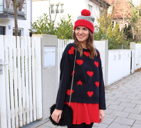 Romantic Holiday Season Look. Fashion Blogger Girl by Style Blog Heartfelt Hunt. Girl with blond, loose waves wearing a romantic sweater with hearts, red skirt, pompom beanie, faux fur bag and over the knee boots.