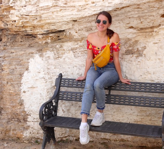 Setenil De Las Bodegas. Fashion Blogger Girl by Style Blog Heartfelt Hunt. Girl with blond, low ponytail wearing a floral off shoulder dress, mom jeans, Ray-Ban sunglasses, yellow belt bag and chunky sneakers.