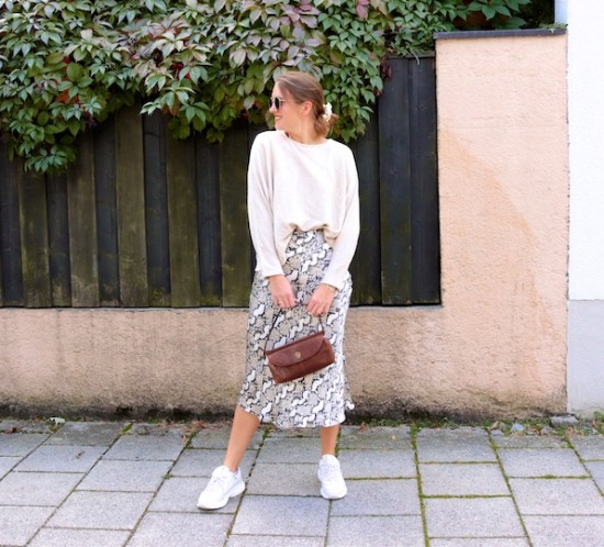 Snake Print Skirt. Fashion Blogger Girl by Style Blog Heartfelt Hunt. Girl with blond low bun wearing a snake print skirt, beige sweater, Ray-Ban sunglasses, scrunchie, baguette bag and chunky sneakers.
