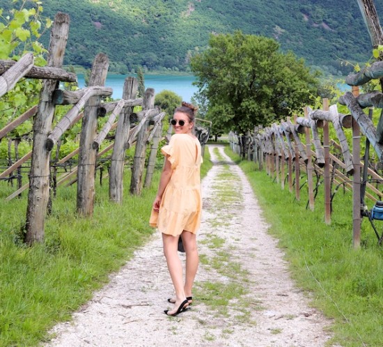 South Tyrol. Fashion Blogger Girl by Style Blog Heartfelt Hunt. Girl with blond high messy bun wearing a yellow gingham dress, Ray-Ban sunglasses, transparent bag with tortoiseshell handles and transparent flats.