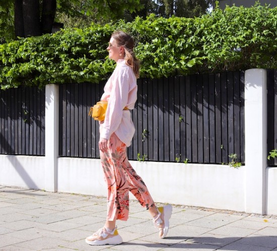 Tropical Flowers. Fashion Blogger Girl by Style Blog Heartfelt Hunt. Girl with blond hair and a pink hair clip wearing pants with tropical flowers, striped shirt, Ray-Ban sunglasses, earrings, yellow belt bag and chunky sneakers.