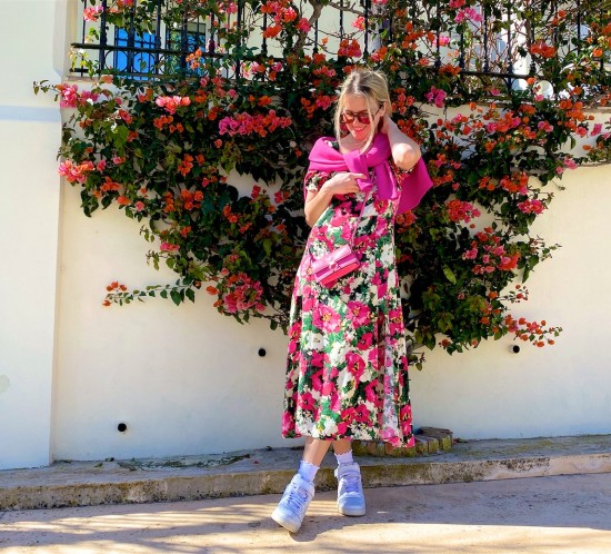 Ultimate Spring Look. Fashion Blogger Girl by Style Blog Heartfelt Hunt. Girl with blond hair wearing a pink sweater, floral dress, sunglasses, pink mini bag and white Nike sneakers.